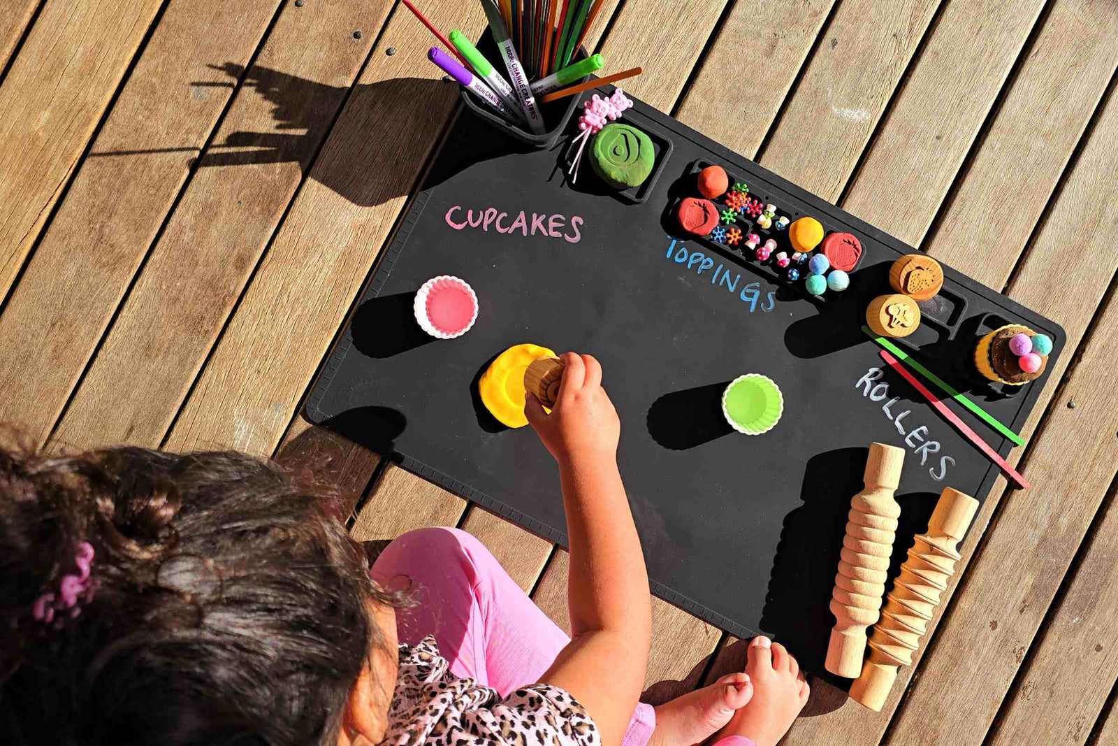 A child engaging in creative, open-ended play using a black silicone craft mat and a variety of art supplies.