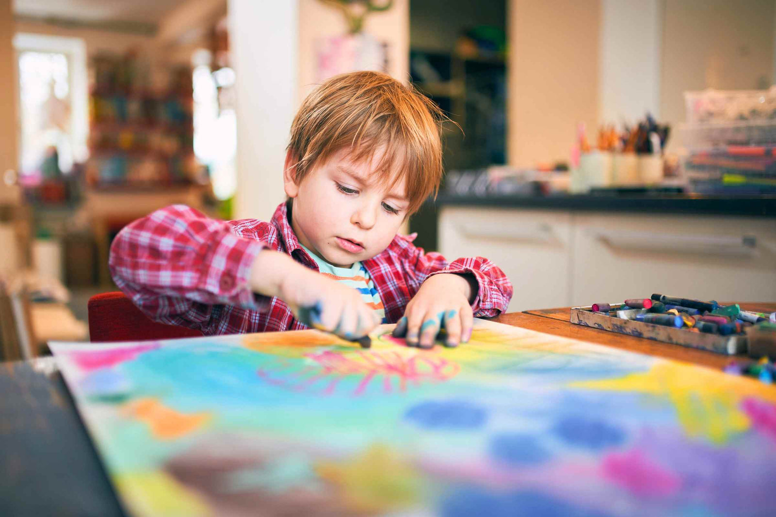A young boy sitting at a table drawing a colourful picture using pastels.