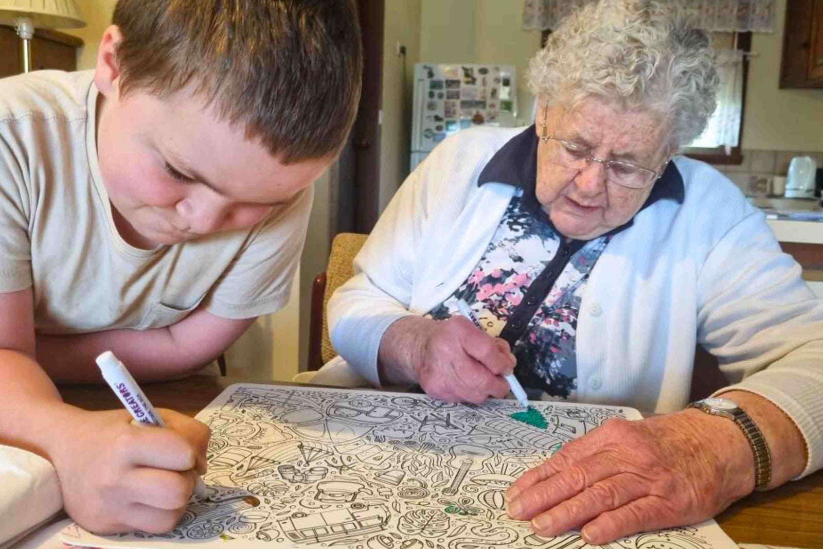 An elderly lady and young boy enjoy colouring a silicone mat together.