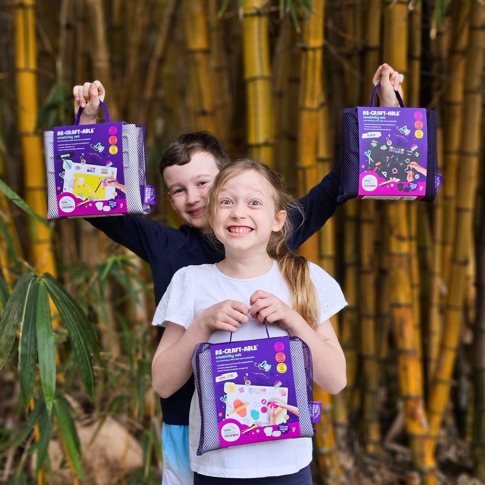 An excited boy and girl holding three Re-CRAFT-able Creativity Sets in purple packaging.