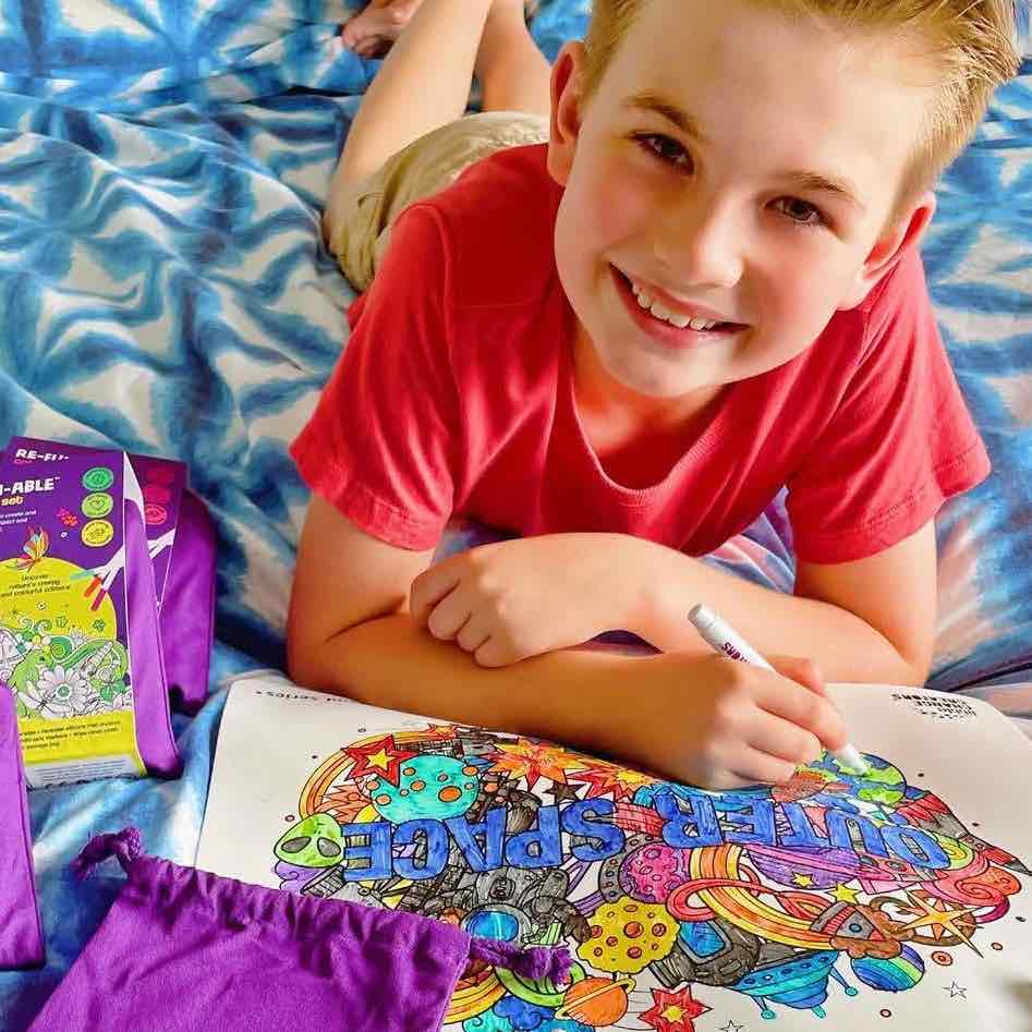 Image of a young boy wearing a red shirt lying down and colouring in the Little Change Creators Outer Space reusable colouring mat.