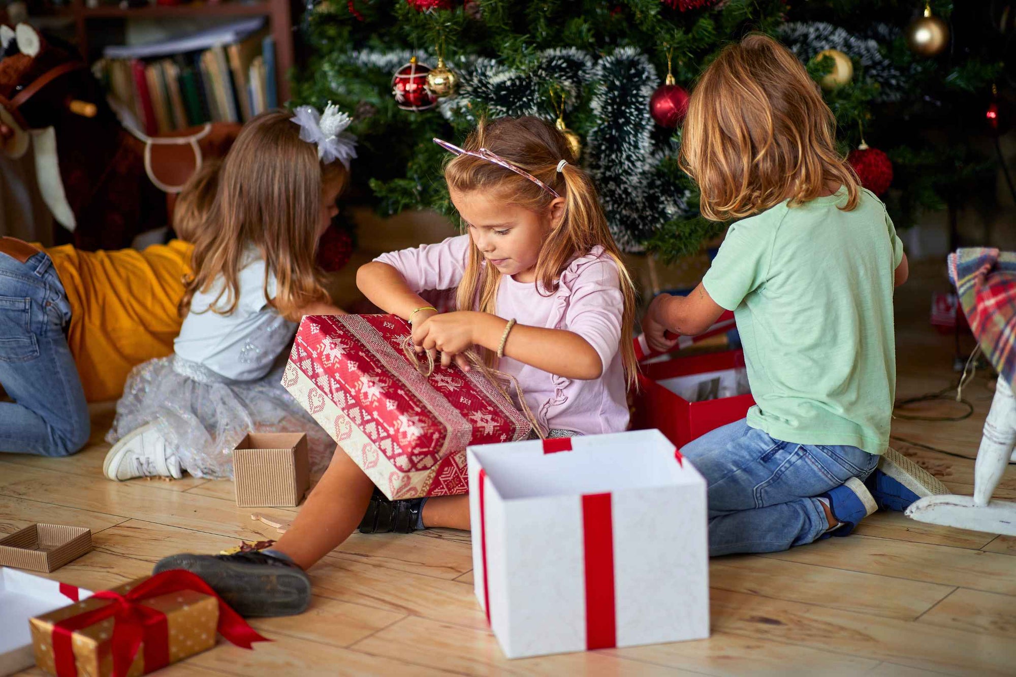 Children gathered around a Christmas tree opening eco-friendly gifts for kids