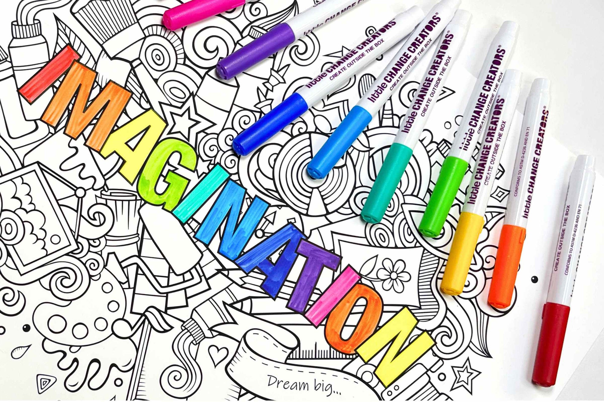 A silicone colouring mat with the word IMAGINATION in rainbow colours.  Multi-coloured marker pens are also scattered on the right side of the image.