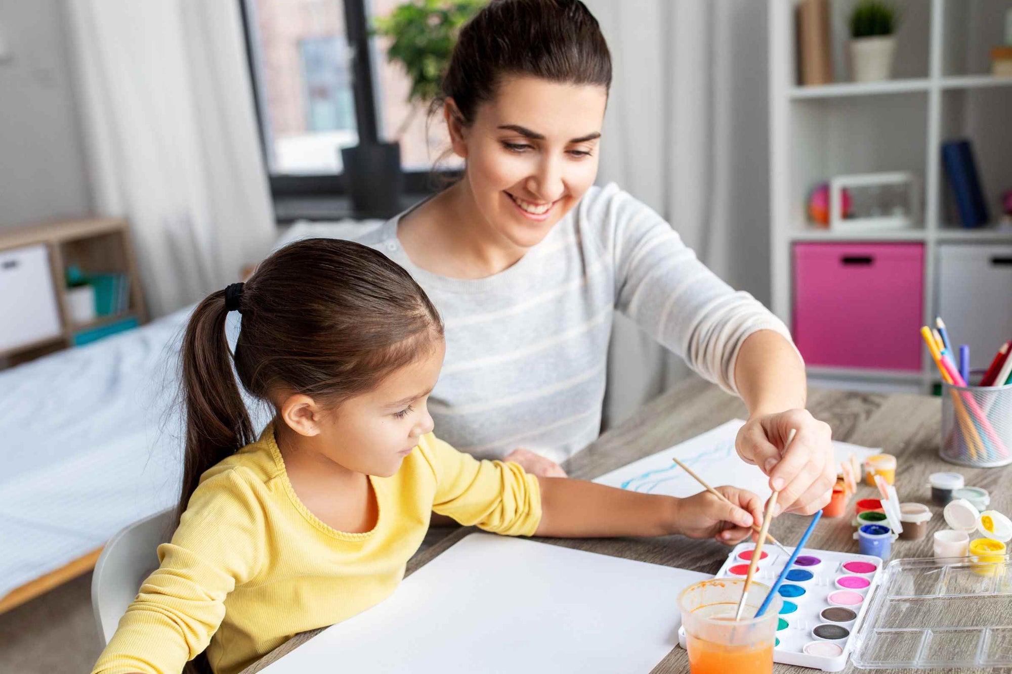 A mother engages her daughter in an open-ended creative activity involving a painting kit.