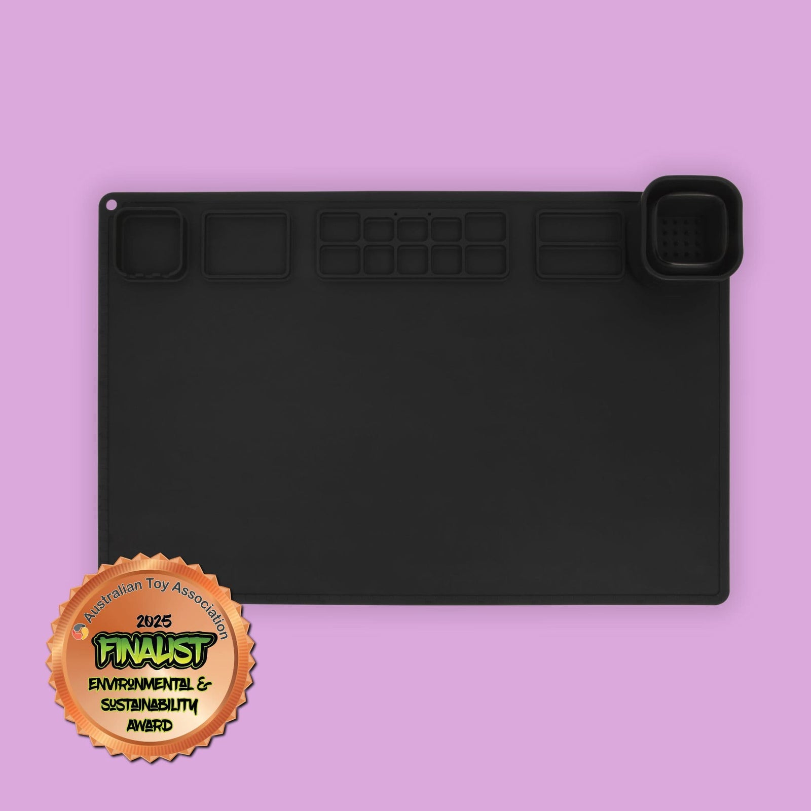A black silicone painting mat with collapsible cup and in-built palette. Image includes the Australian Toy Association Environmental and Sustainability Award.