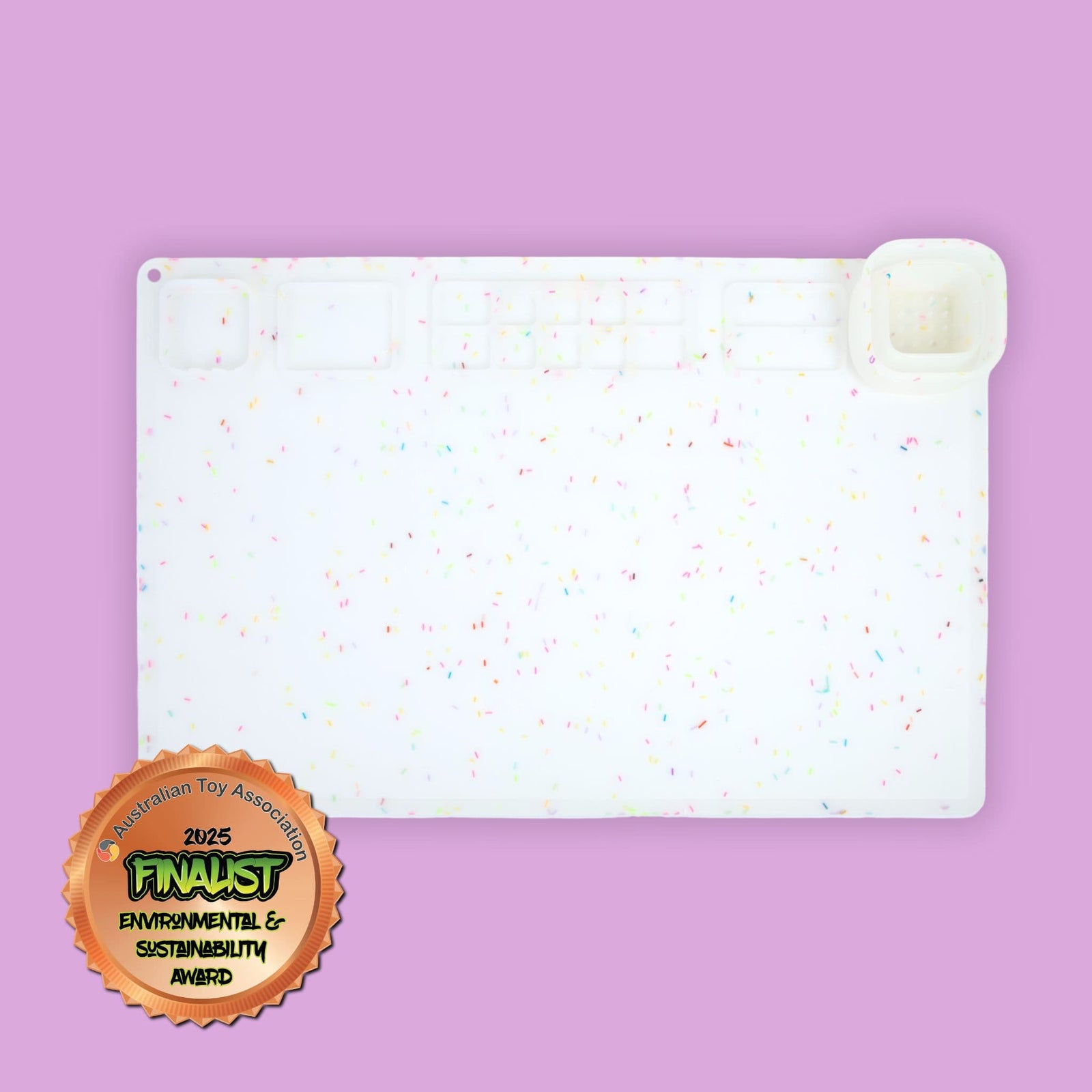 A white silicone art and craft mat with multi-coloured sprinkles pattern. Image includes the Australian Toy Association Environmental & Sustainability Award.