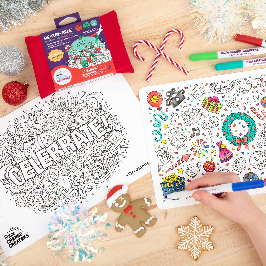 Christmas-themed silicone placemats with colouring markers and Christmas decorations on a wooden table top.