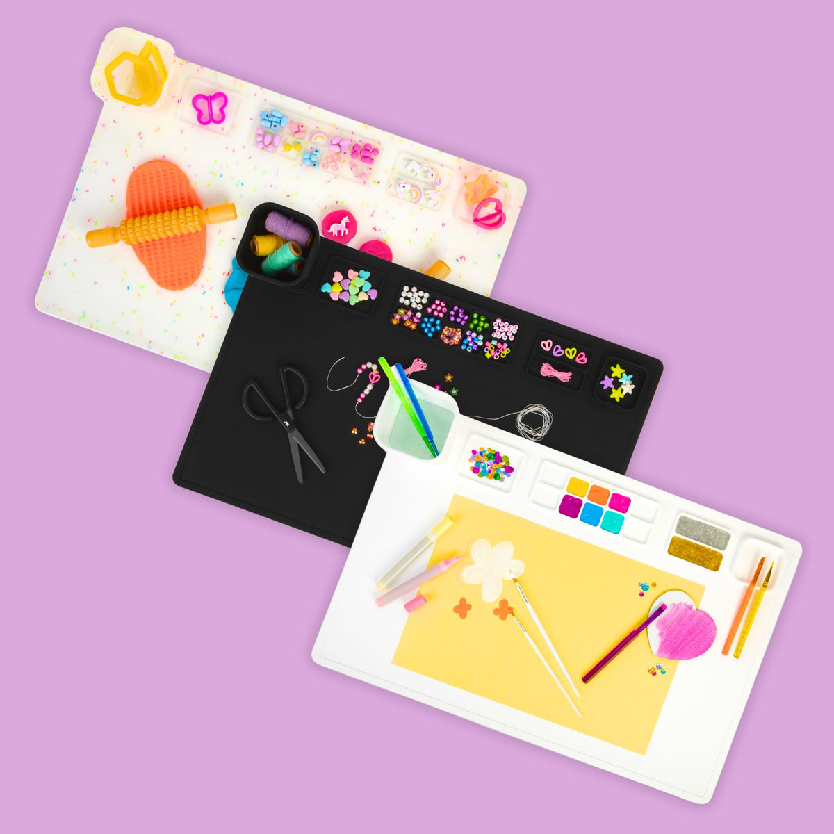 Three Re-CRAFT-able silicone art, craft and sensory activity mats on a mauve background.  Image shows a white mat, a black mat and a multi-coloured confetti mat.  Each mat demonstrates a type of activity, such as painting, jewellery-making and modelling with play dough.