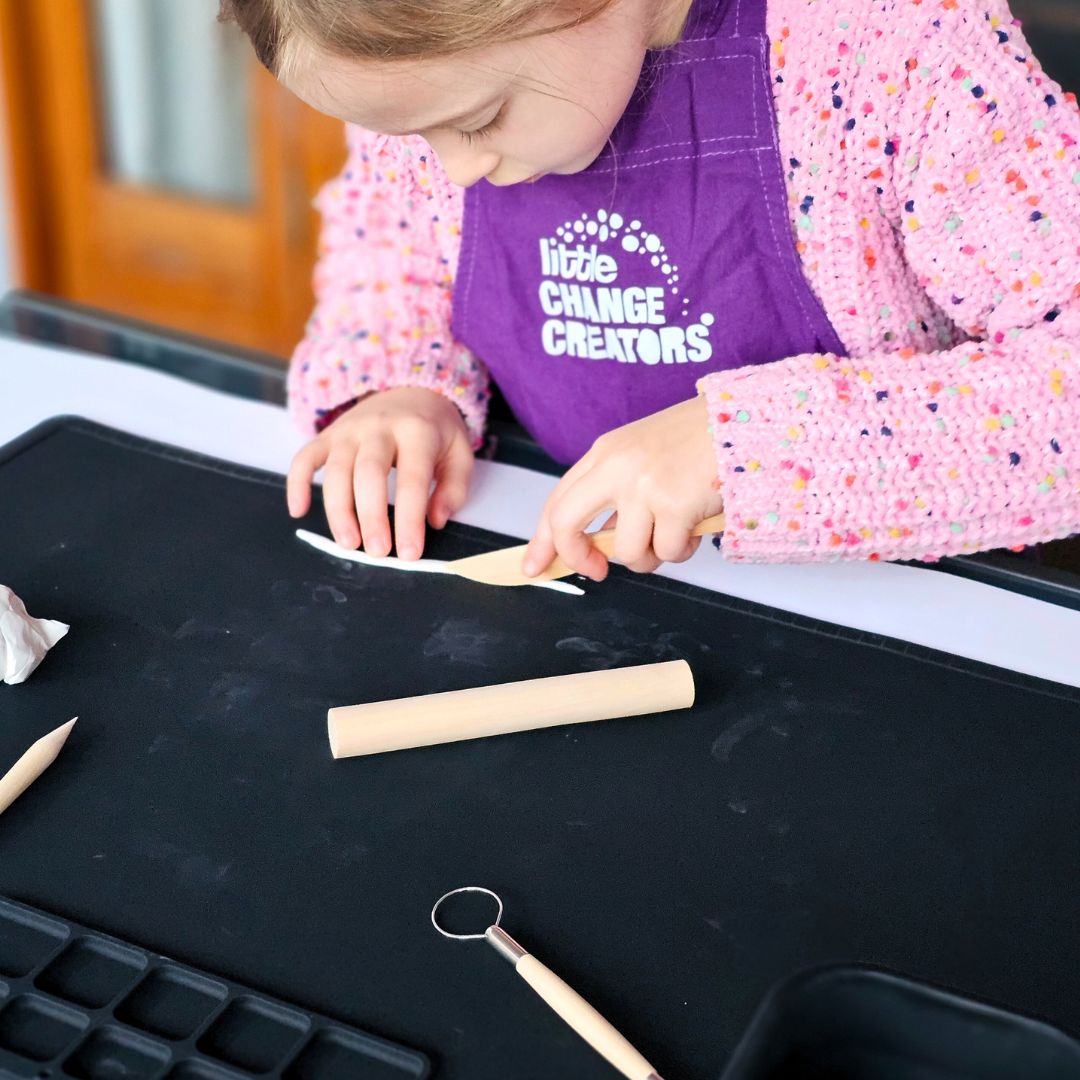 Kids clay modelling kit with gift packaging, wooden tools, and a block of clay on a pink background.