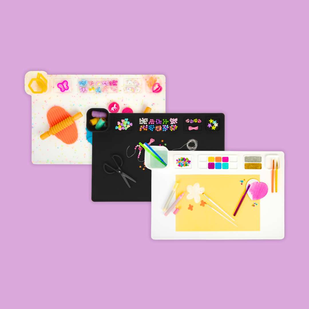 Three Re-CRAFT-able silicone art, craft and sensory activity mats on a mauve background.  Image shows a white mat, a black mat and a multi-coloured confetti mat.  Each mat demonstrates a type of activity, such as painting, jewellery-making and modelling with play dough.