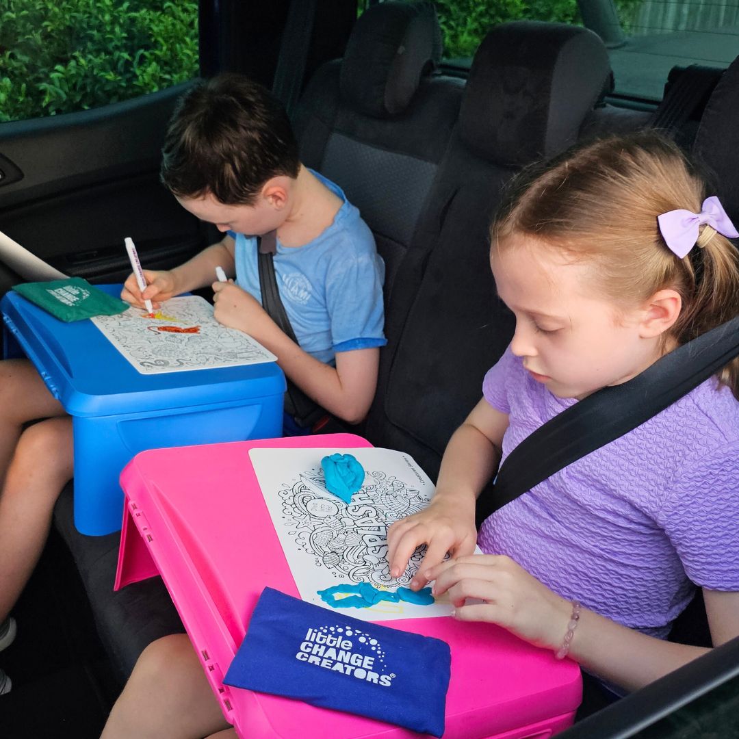 Image shows two children using Little Change Creators reusable colouring mats and silicone activity mats in a car.  The boy is colouring and the girl is using playdough.
