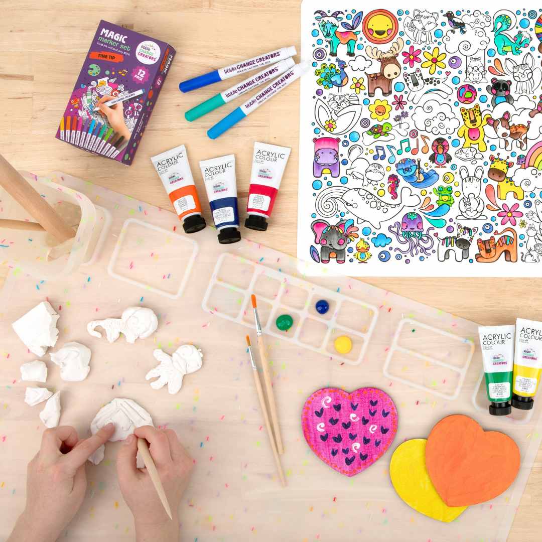 A child's hands using modelling clay with coloured pens, painting supplies and a completed silicone colouring mat on a wooden surface.