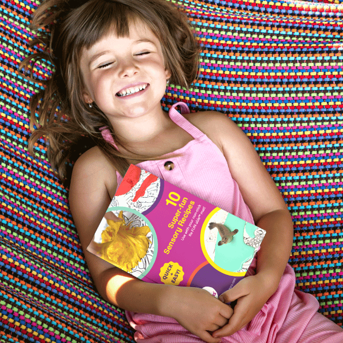 Happy girl holding a book about sensory activities and sensory play ideas for kids